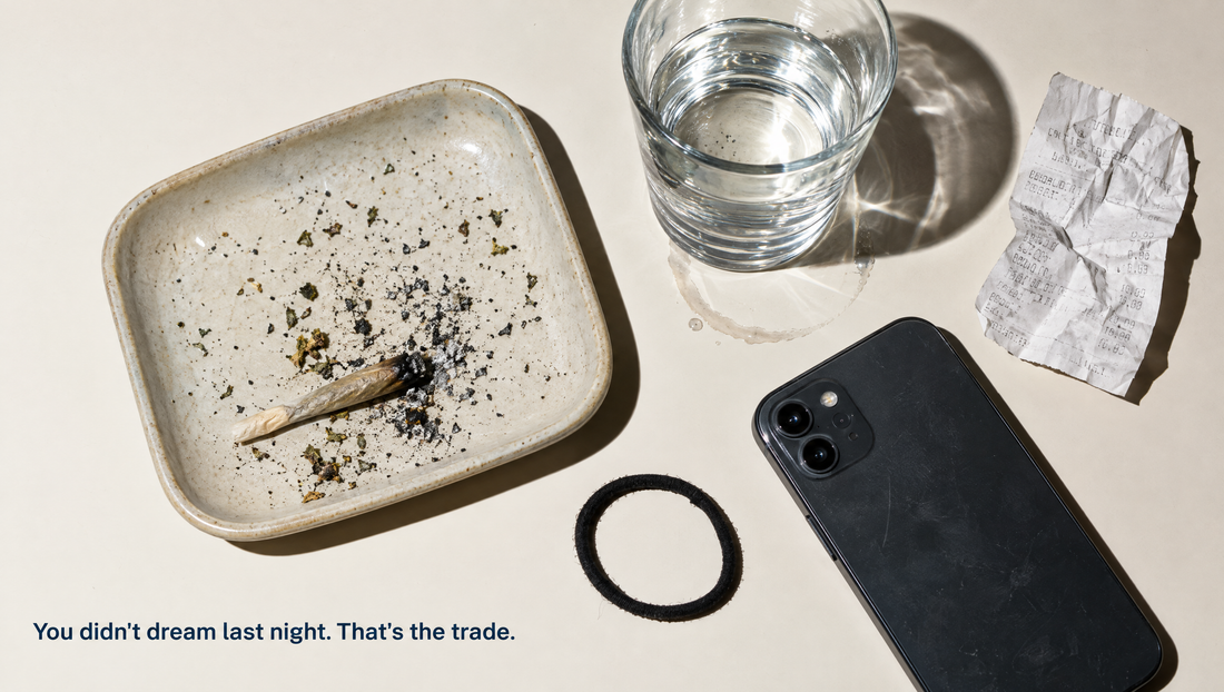 Overhead view of a nightstand at night: a ceramic tray holding a stubbed-out joint and loose ash, a phone lying face down, a glass of water and a hair tie on a pale surface.