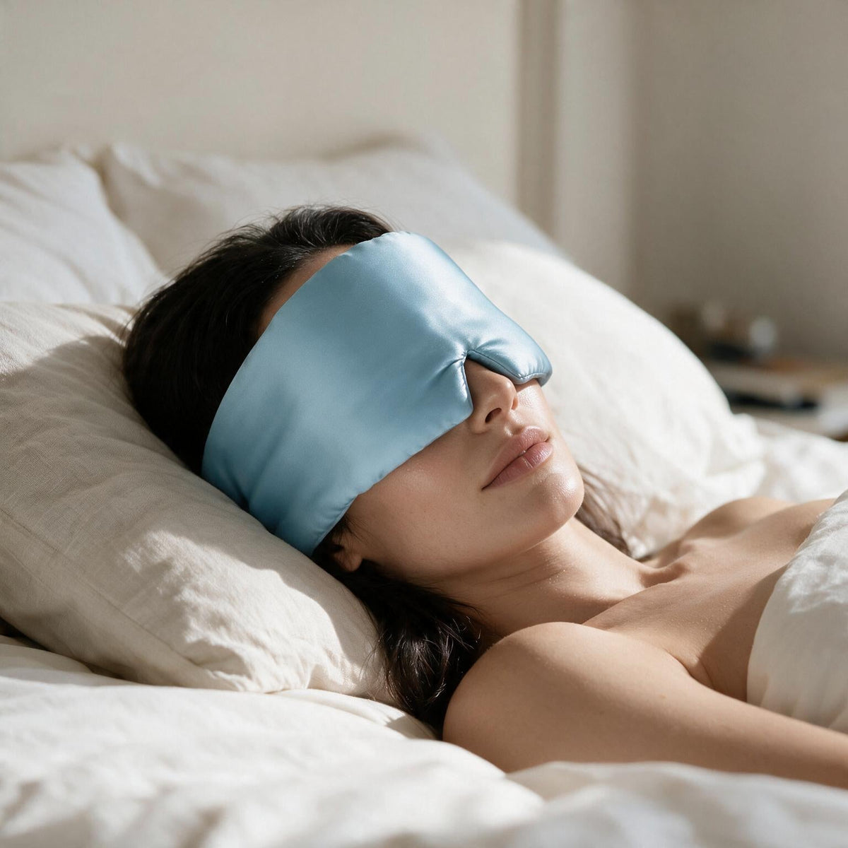 Woman asleep on her back wearing the Lunia Reve silk sleep mask in Sky Blue in soft morning light